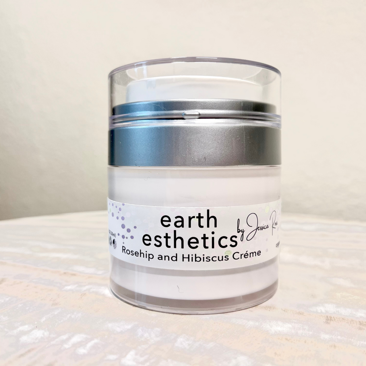A jar of earth esthetics Rosehip and Hibiscus Crème, with a white label on a textured background.